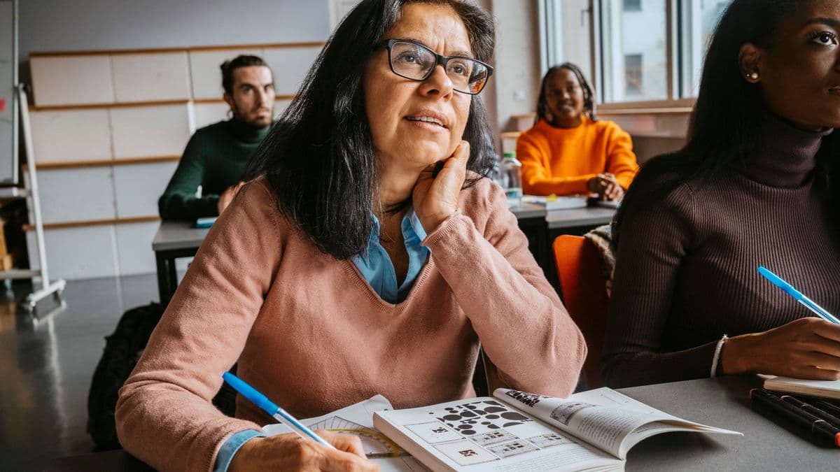 An adult learner sat at a classroom table with pen and activity book.