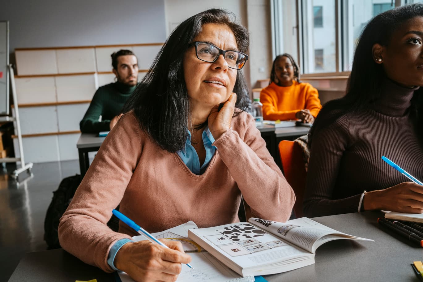 An adult learner sat at a classroom table with pen and activity book.