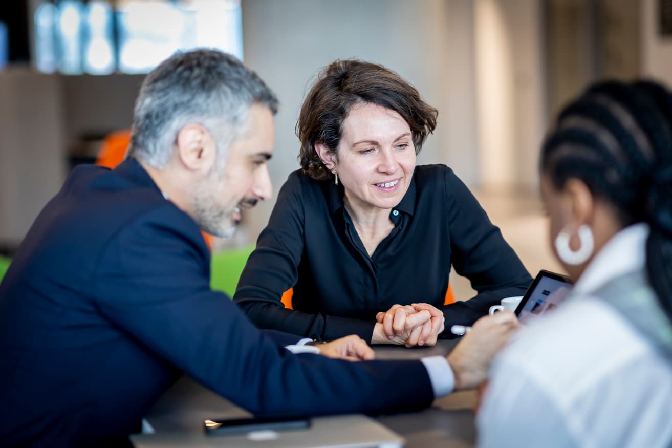 A man and two women sat at a table around an iPad in discussion.