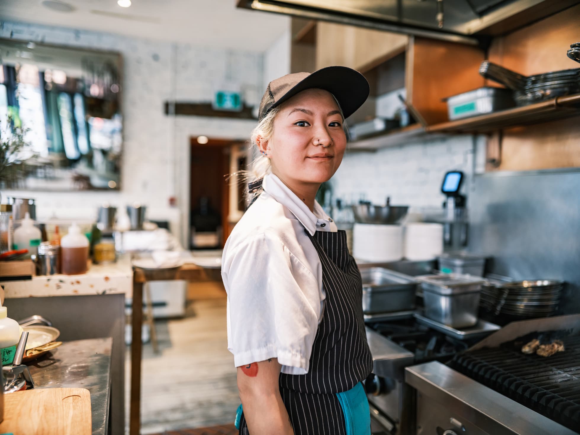 A young person wearing chef's whites and an apron in a kitchen.