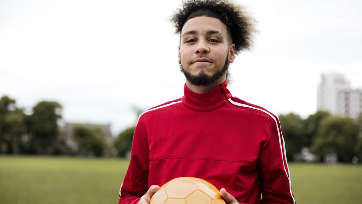Young man holding a football in a park.