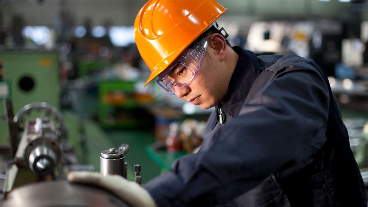 Technician in uniform and hard hat working on a machinery.